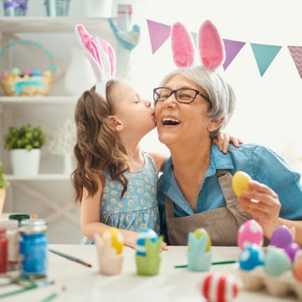 Enkeltochter gibt Oma einen Kuss, beide tragen Hasenohren.