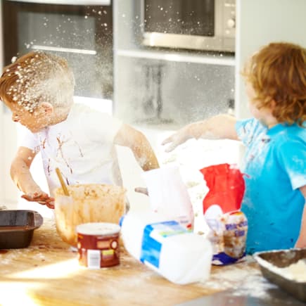 Zwei Kinder streiten beim Backen und bewerfen sich mit Mehl.