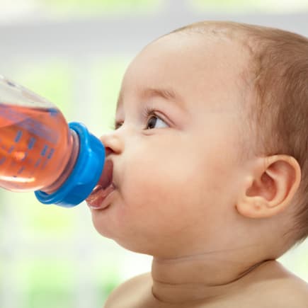 Baby trinkt Tee aus Nuckelflasche.