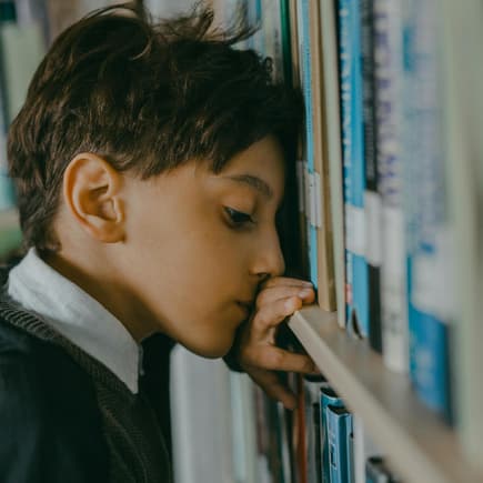 Nachdenklicher Junge lehnt Kopf gegen Bücherregal.