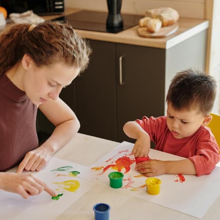 Mutter und Kind malen mit Fingerfarbe auf Papier.