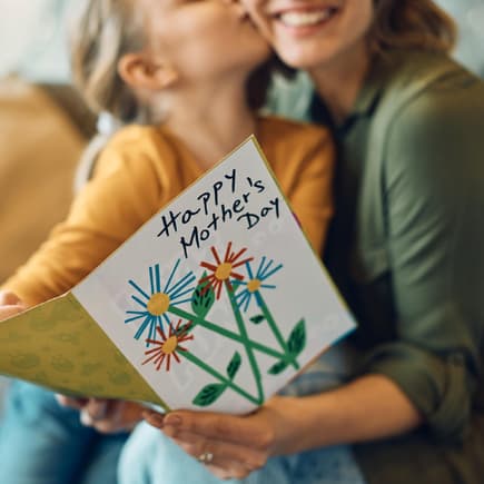 Kind küsst Mutter und schenkt ihr eine Karte zum Muttertag.