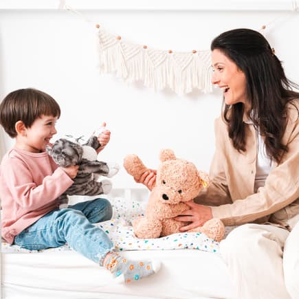 Mutter und Kind spielen auf Bett mit Kuscheltieren.