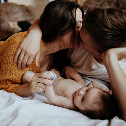 Eltern kuscheln mit Neugeborenem.