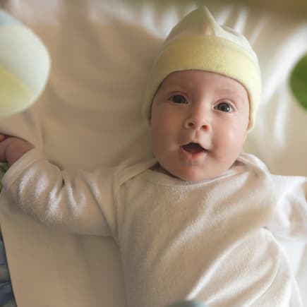 Baby liegt fröhlich unter einem Mobile.