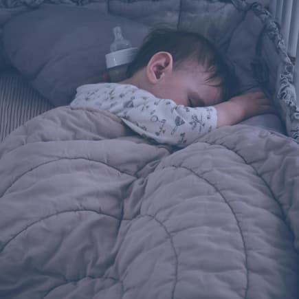 Baby im Bett mit Nestchen und Decke.