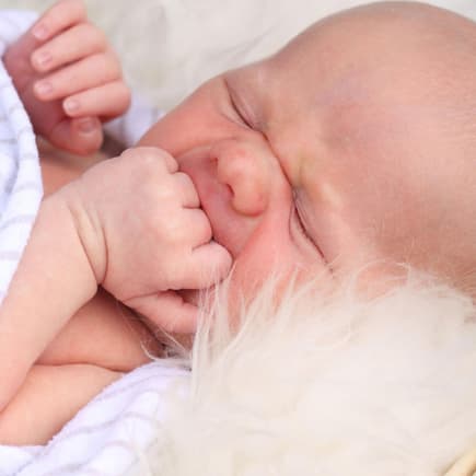 Baby liegt bei sommrlichen Temperaturen auf einem Lammfell
