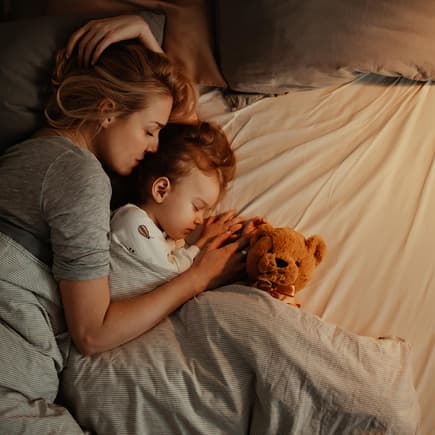 Mutter liegt mit kleinem Kind im Bett.