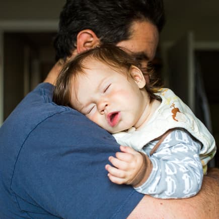 Baby schläft auf Papas Arm.