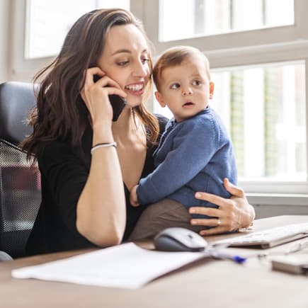 Mutter arbeitet mit Kind auf dem Schoß.