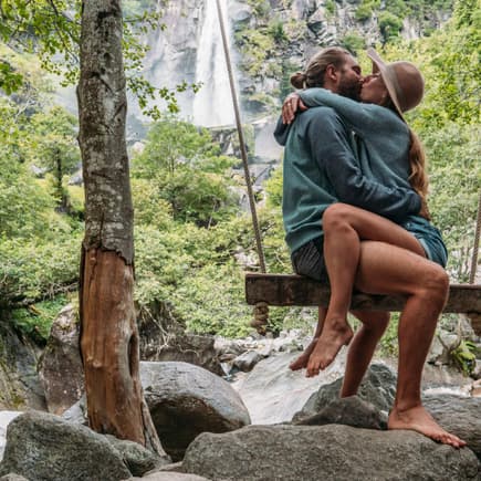 Paar sitzt sich küssend auf einer Schaukel in der Natur.