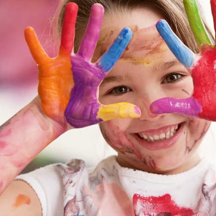 Fröhliches Kind mit bunten Fingerfarben an den Händen.