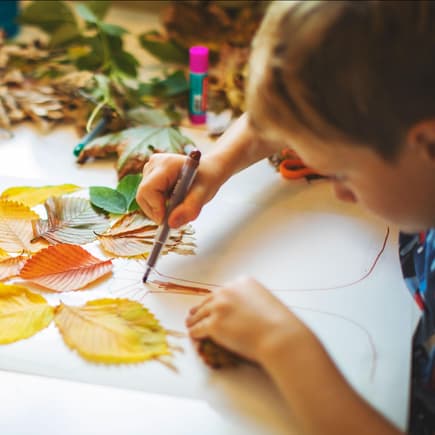 Kinder basteln mit Herbstblättern und Stiften.