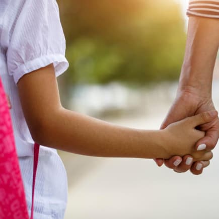 Schulkind an der Hand der Mutter.