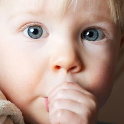 Kleines Kind nuckelt mit großen Augen am Daumen.