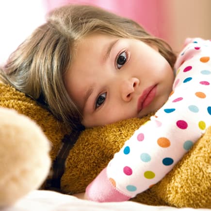 Ein kleines Mädchen schmollt mit seinem Teddy auf dem Bett.