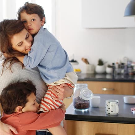 Mutter kuschelt in der Küche mit ihren beiden Kindern.