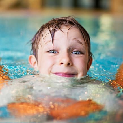 Kind mit Schwimmnudel im Wasser.