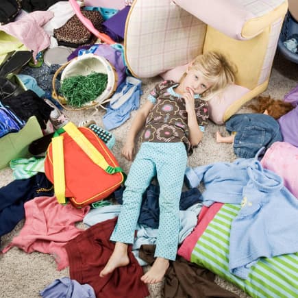 Kind liegt in chaotischem Kinderzimmer auf dem Boden.