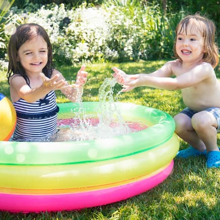 Zwei kleine Mädchen spielen in einem Planschbecken im Garten.