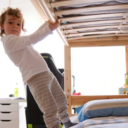 Ein Hochbett bedeutet viel Spaß, aber birgt auch ein Risiko für Kinder. Kind steht unten auf Hochbett.