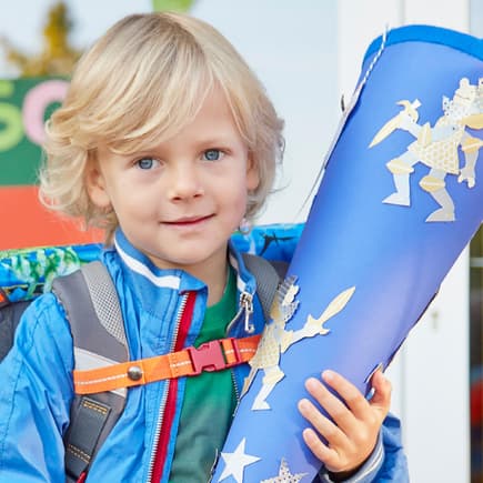 Ein kleiner Junge hat seinen Schulranzen auf und hält stolz seine Schultüte fest.