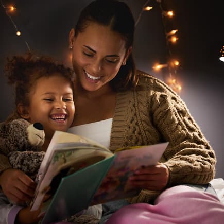 Mutter und Kind lachen beim abendlichen Vorlesen.