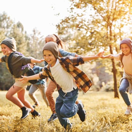 Kinder laufen fröhlich über eine herbstliche Wiese.