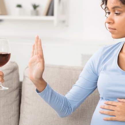 Schwangere Frau lehnt ein Glas Wein ab.