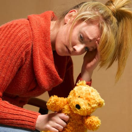 Erschöpfte, mutlose Frau mit Teddy in der Hand.