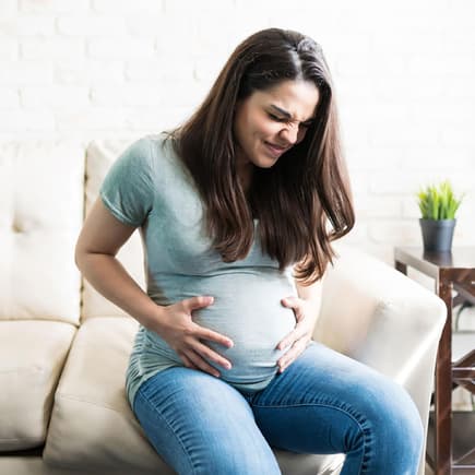 Eine schwangere Frau mit schmerzverzerrtem Gesicht hält ihren Babybauch. 