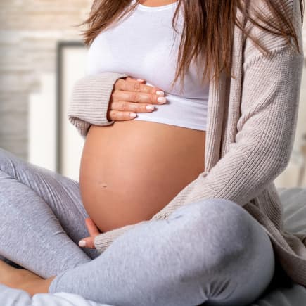 Schwangere Frau sitzt im Schneidersitz und hält sich den Bauch.
