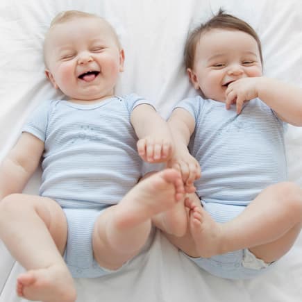 Baby-Zwillinge liegen nebeneinander und lachen.