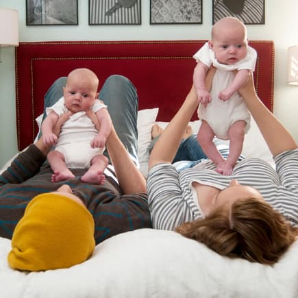 Mutter und Vater liegen auf dem Bett und halten ihre Zwillinge in den Händen.