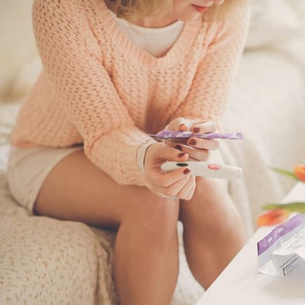 Frau sitzt vor Blumenstrauß mit Ovulationstest in der Hand.
