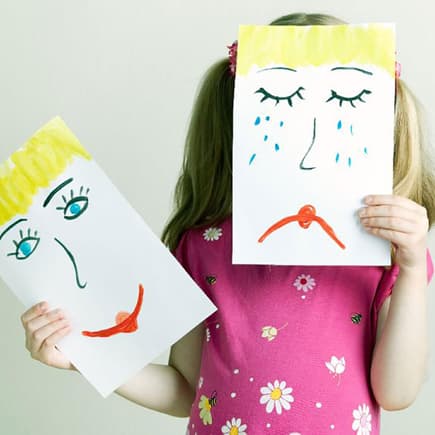 Gefühle zeigen: Kind hält gemaltes, trauriges Gesicht vor ihr eigenes.