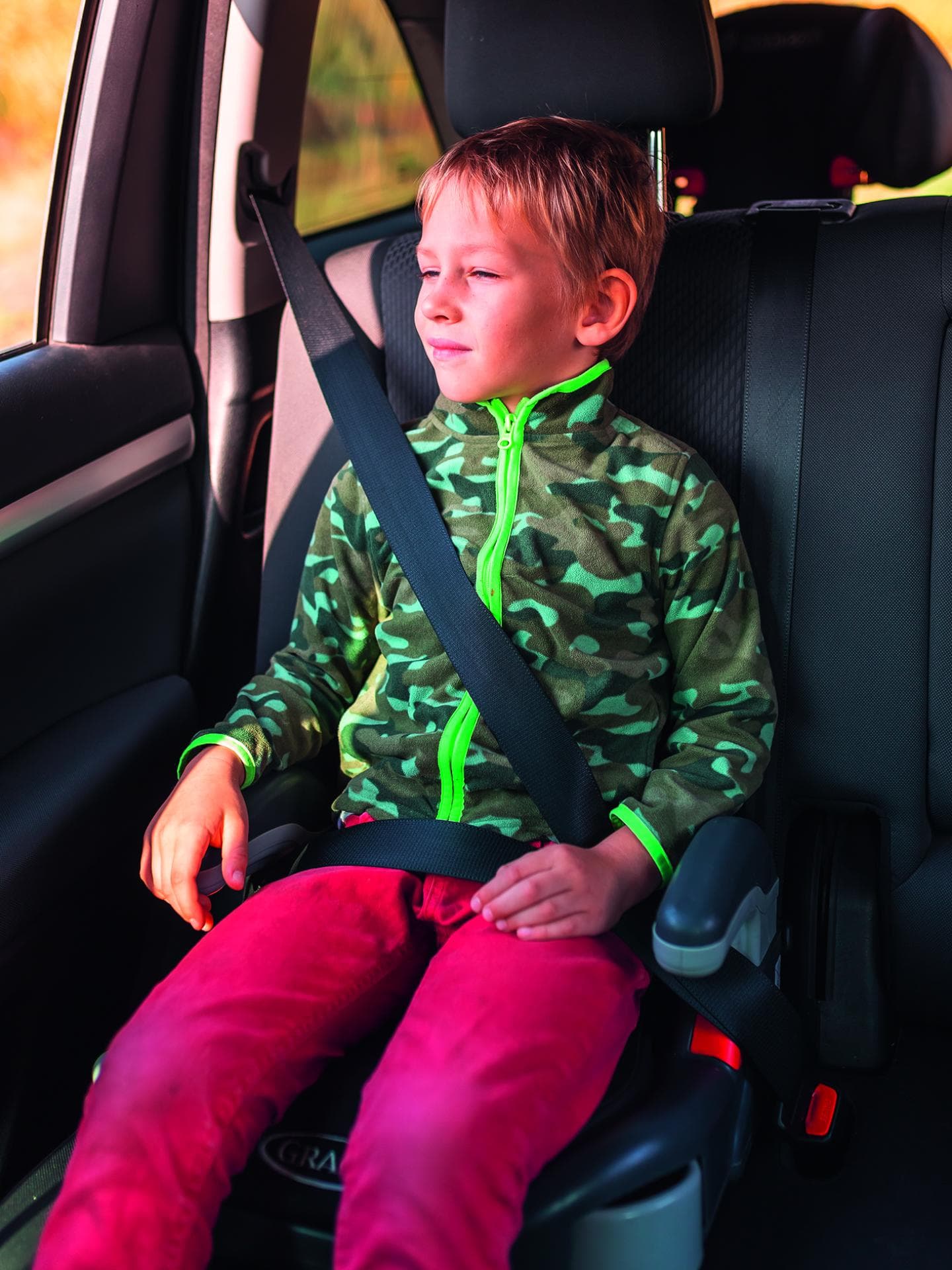Eine Junge sitzt im Auto auf einer Sitzerhöhung. 