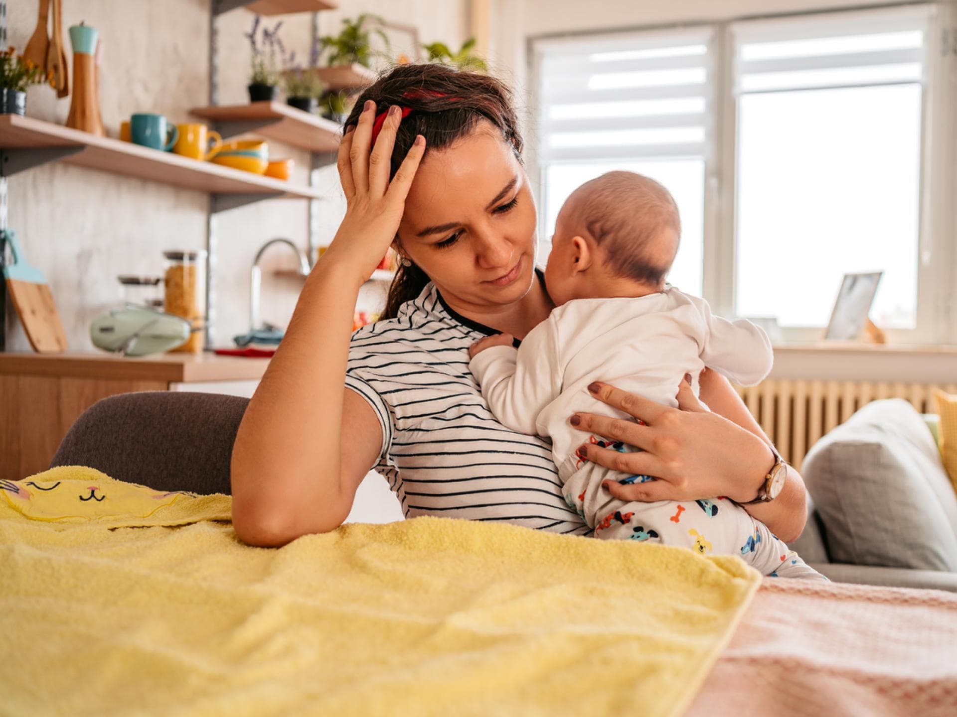 Manche Glaubenssätze sind überflüssig: Junge Mutter mit Baby auf dem Arm fasst sich an den Kopf Junge Mutter mit Baby auf dem Arm fasst sich an den Kopf