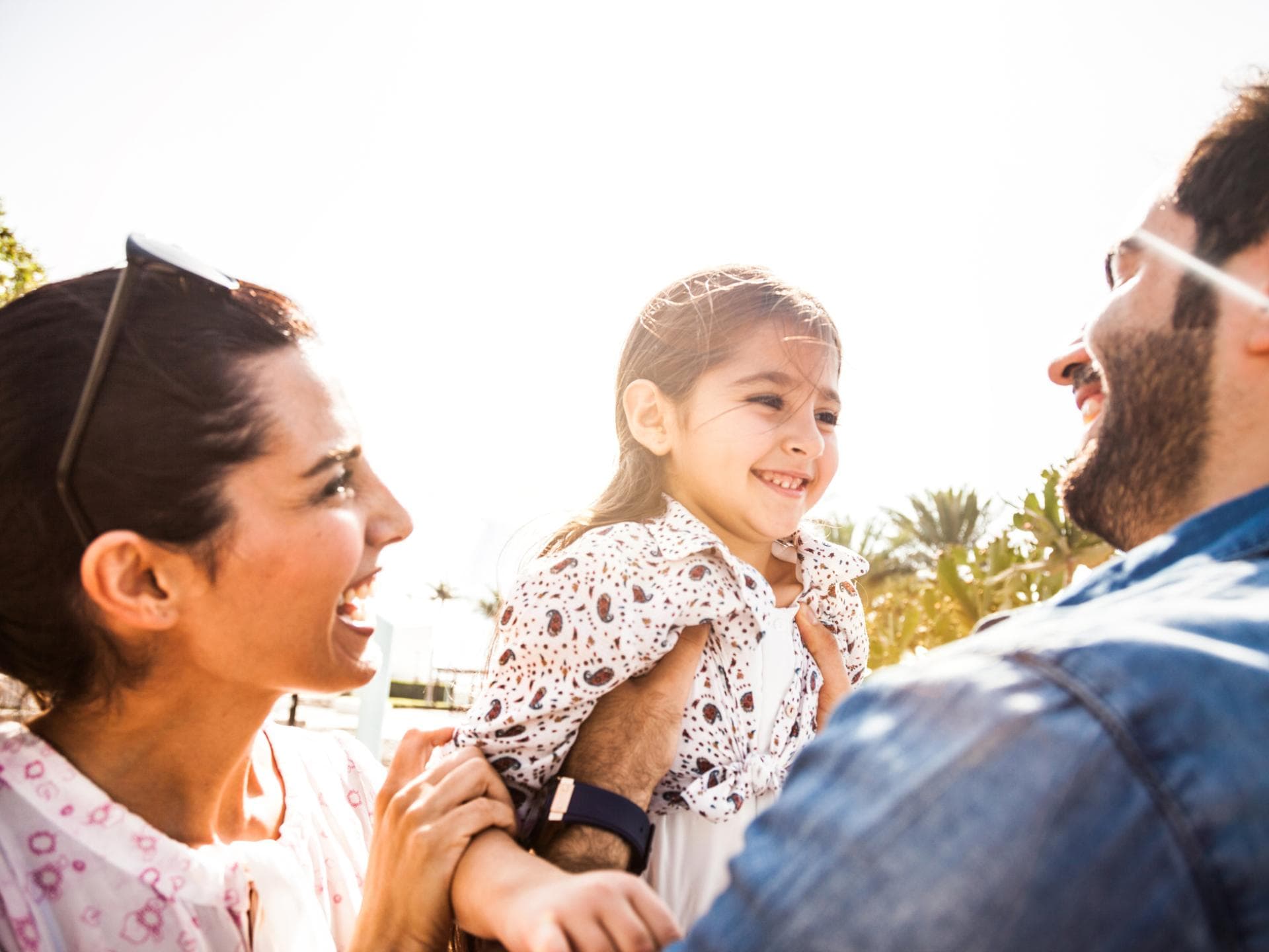 Arabische Mädchennamen klingen oft außergewöhnlich und wunderschön. Mutter und Vater halten ihre lachende Tochter.