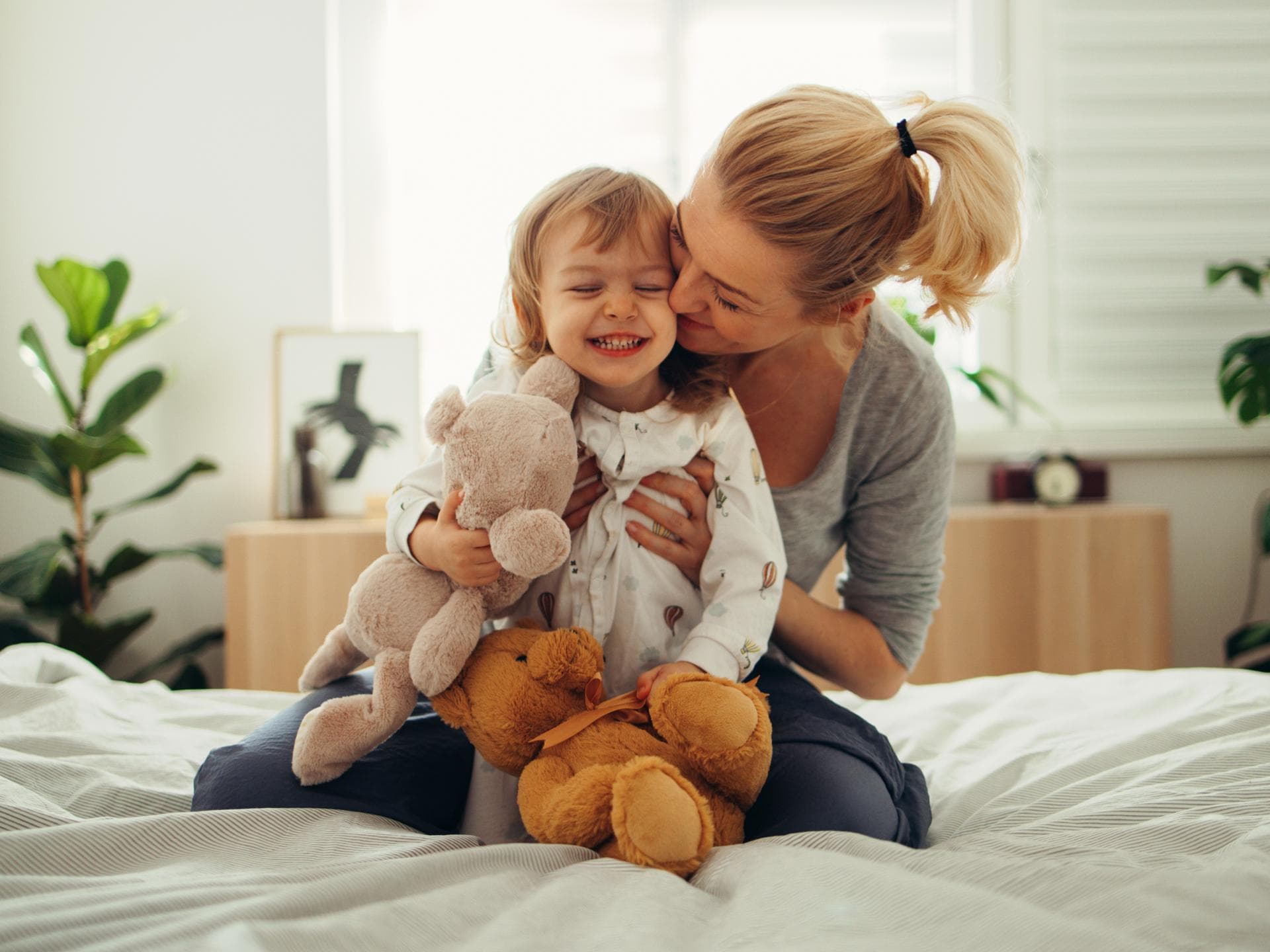 Mama umarmt Mädchen mit Kuscheltieren