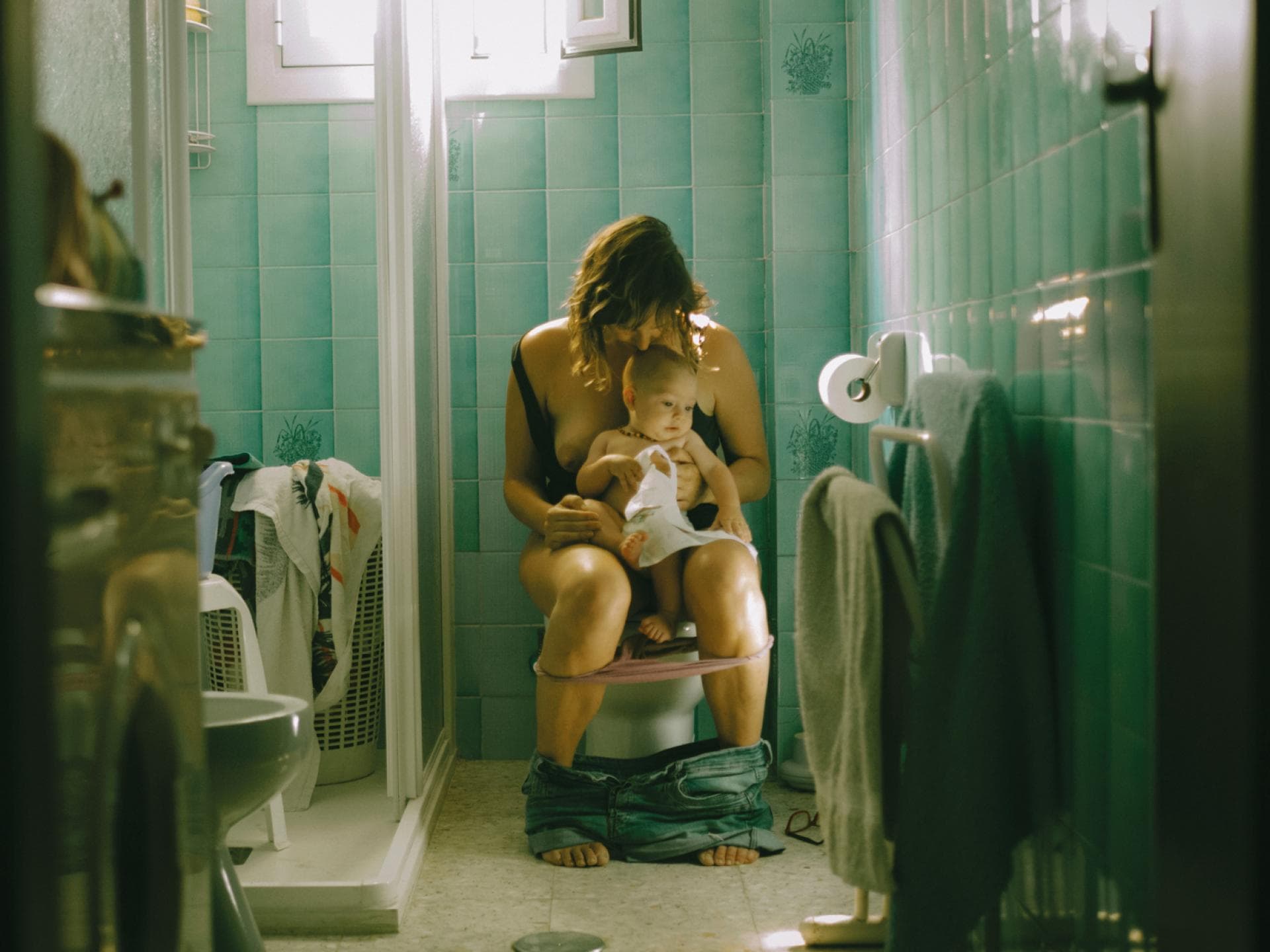 Eine Mutter sitzt übermüdet auf der Toilette mit ihrem Baby auf dem Schoß