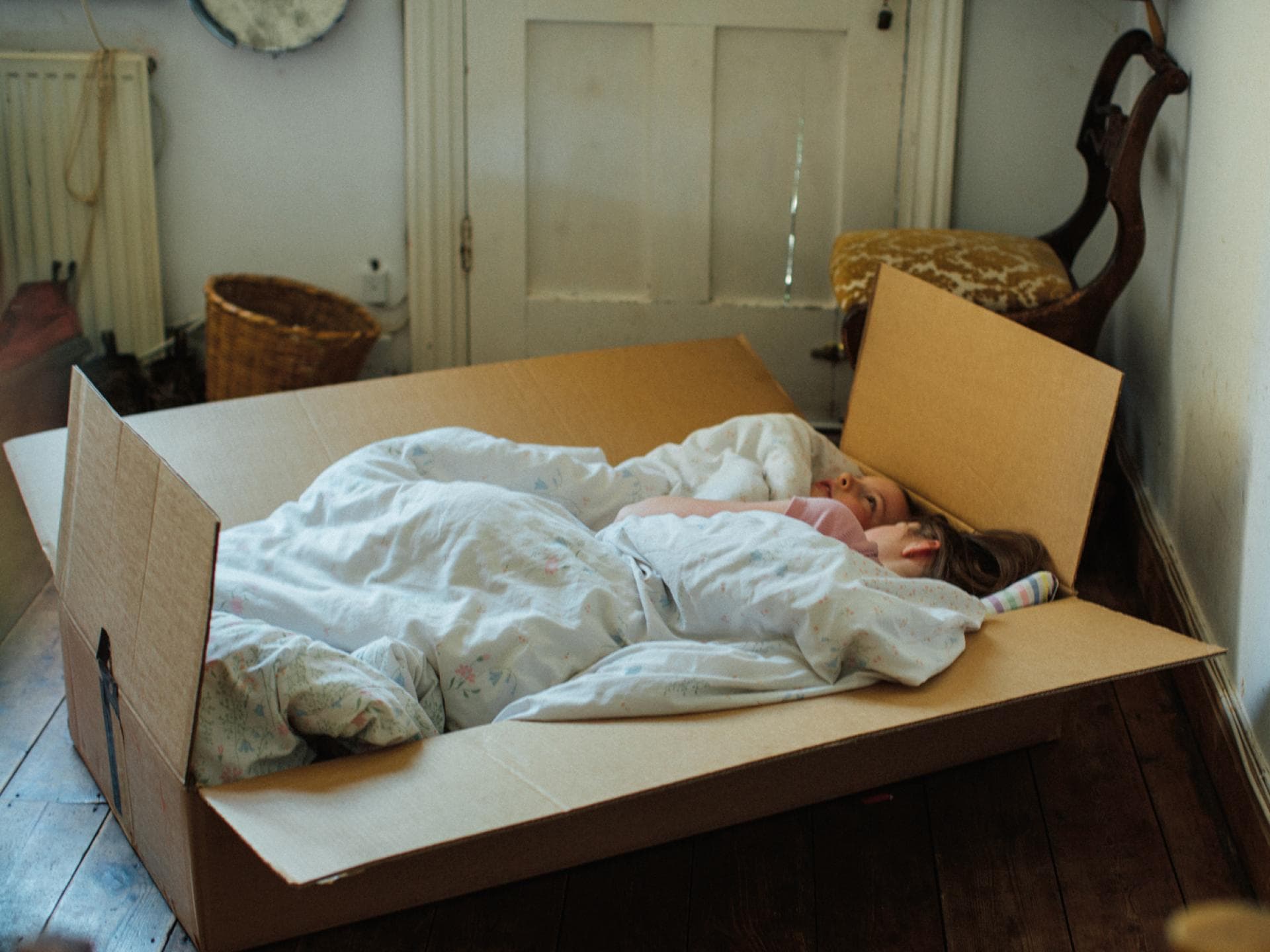 Zwei Kinder kuscheln sich in ein selbstgebautes Bett in einem Karton