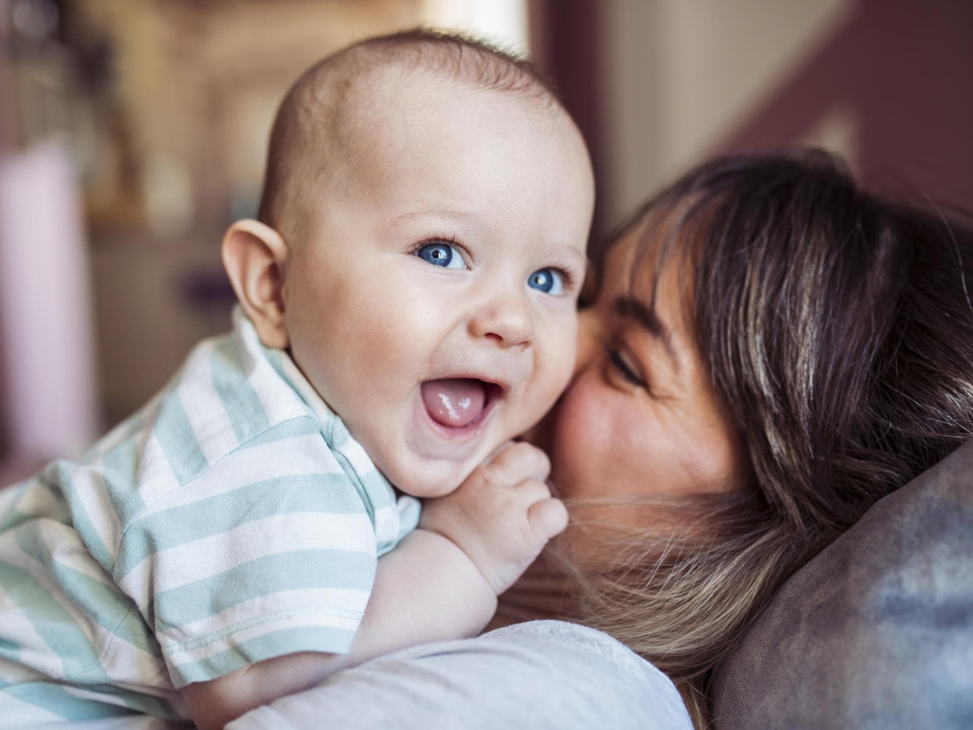 Von Hannes bis Henry: Hier kommen die schönsten Jungennamen mit H. Ein Baby liegt lachend auf seiner Mutter.