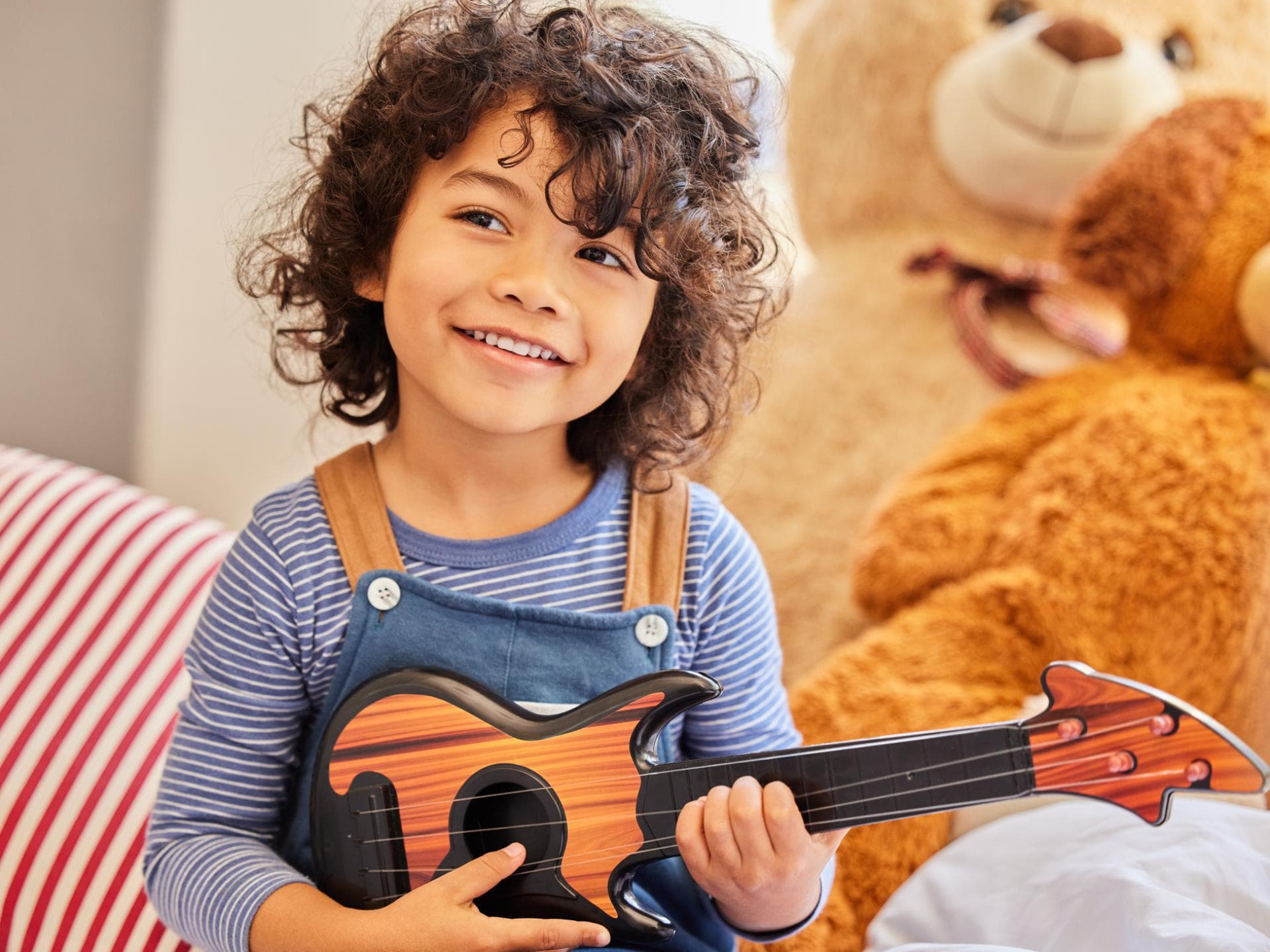 Arabische Jungennamen klingen einzigartig. Ein Junge mit dunklen Locken sitzt mit seiner Gitarre im Kinderzimmer.