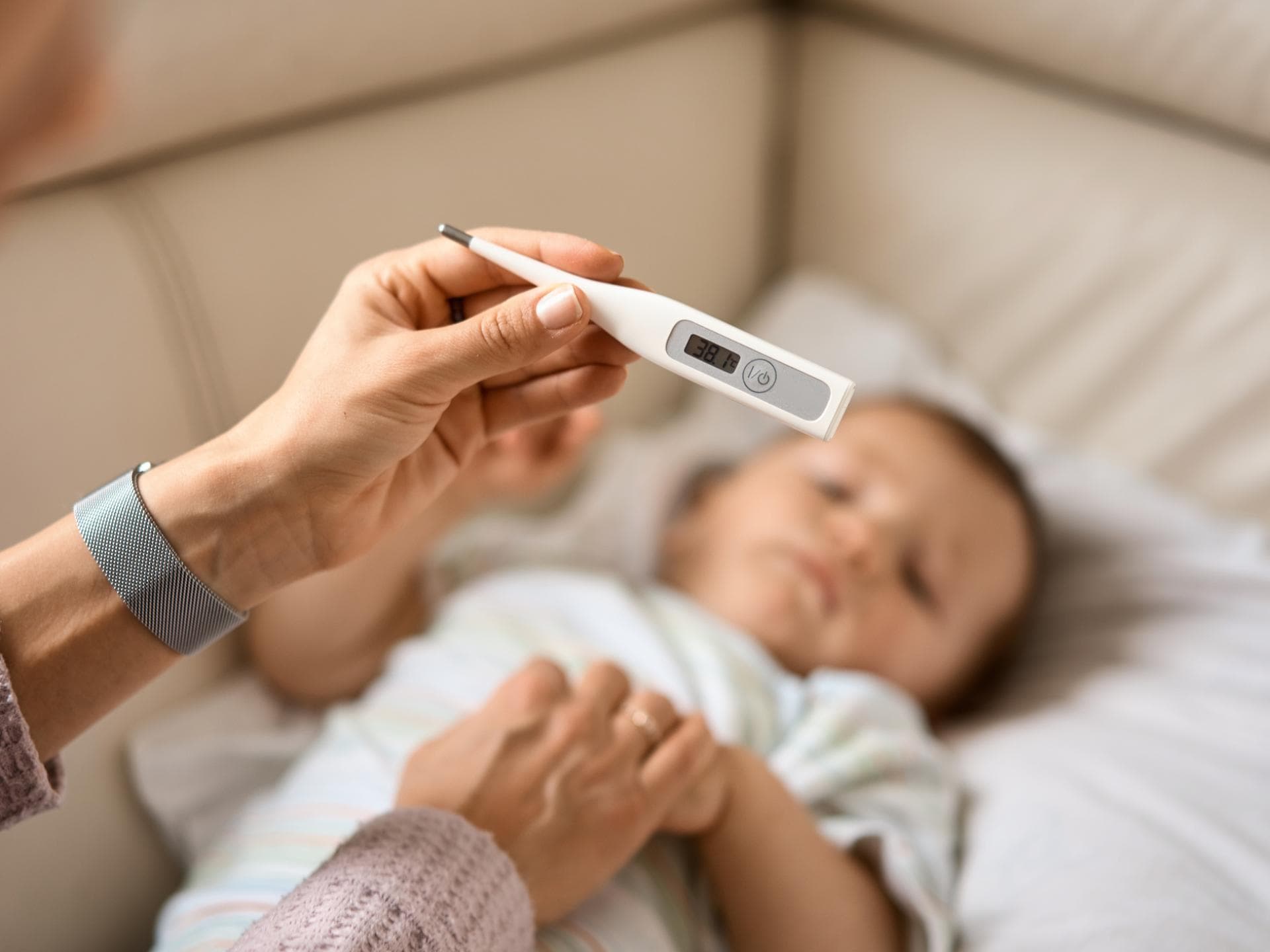 Eine Mutter hält das Fieberthermometer über ihrem Baby.