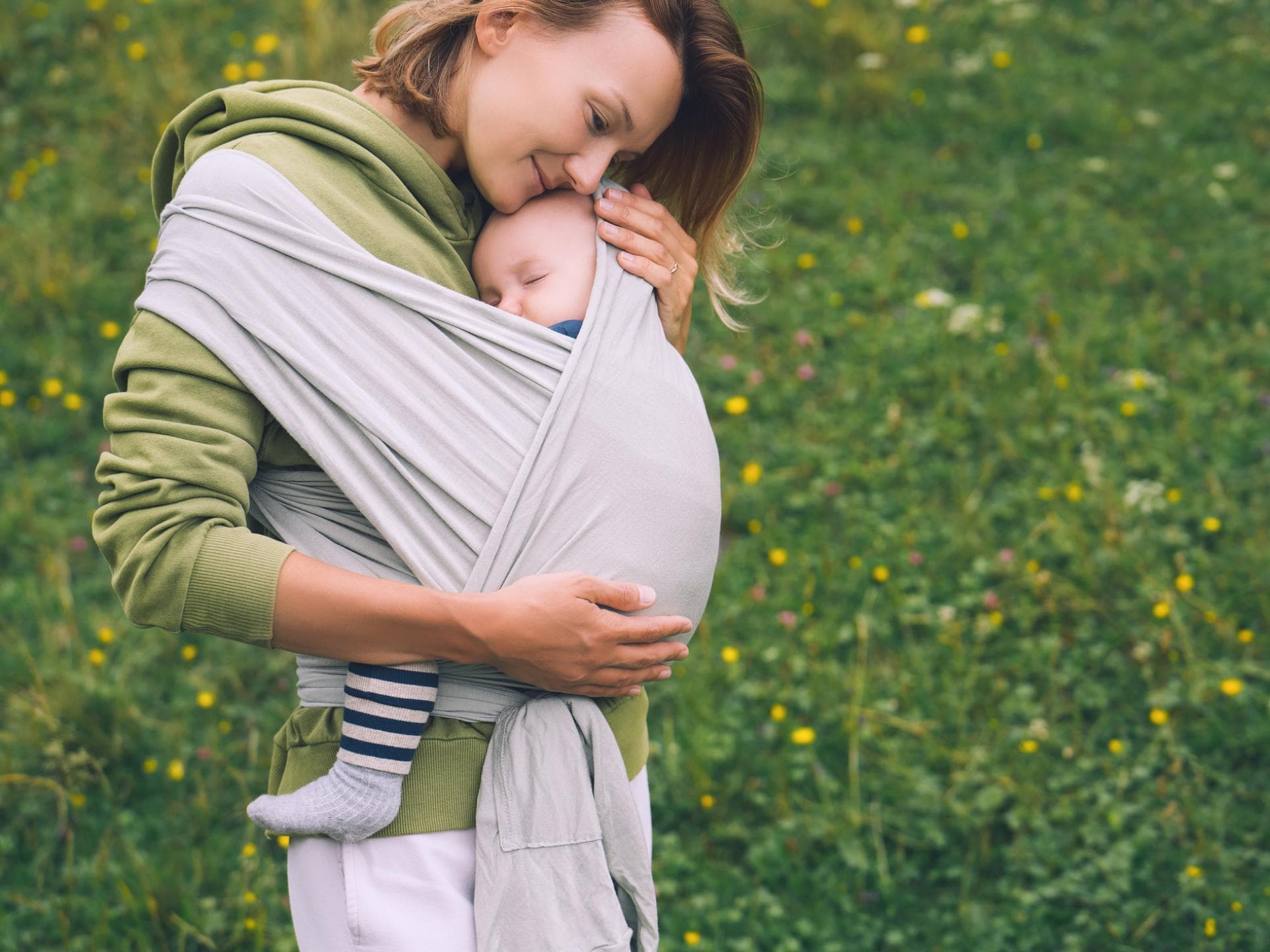 Frau trägt ihr Baby in einer Trage.