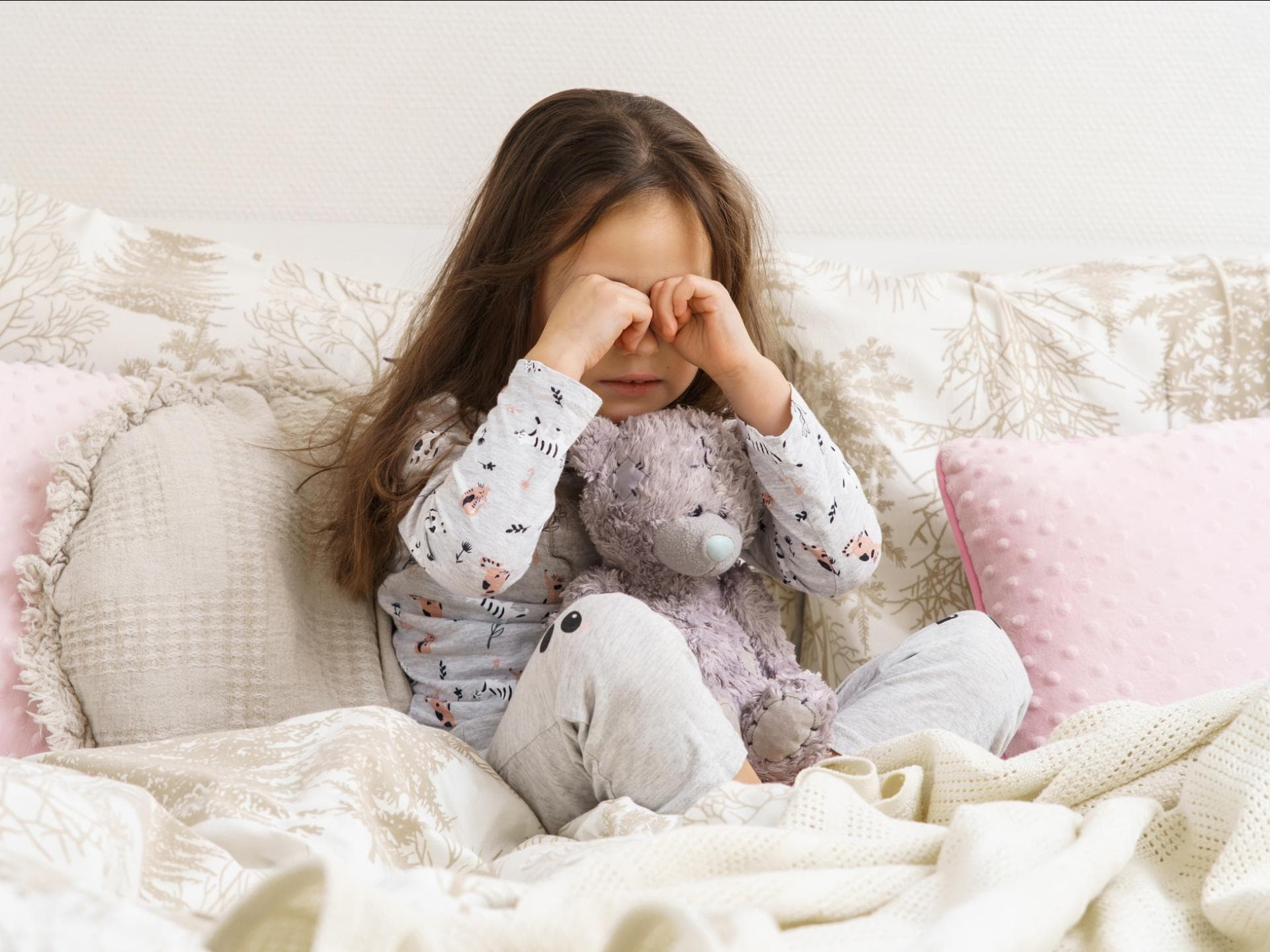 Mädchen sitzt im Schlafanzug auf dem Bett und weint Mädchen sitzt im Schlafanzug auf dem Bett und weint