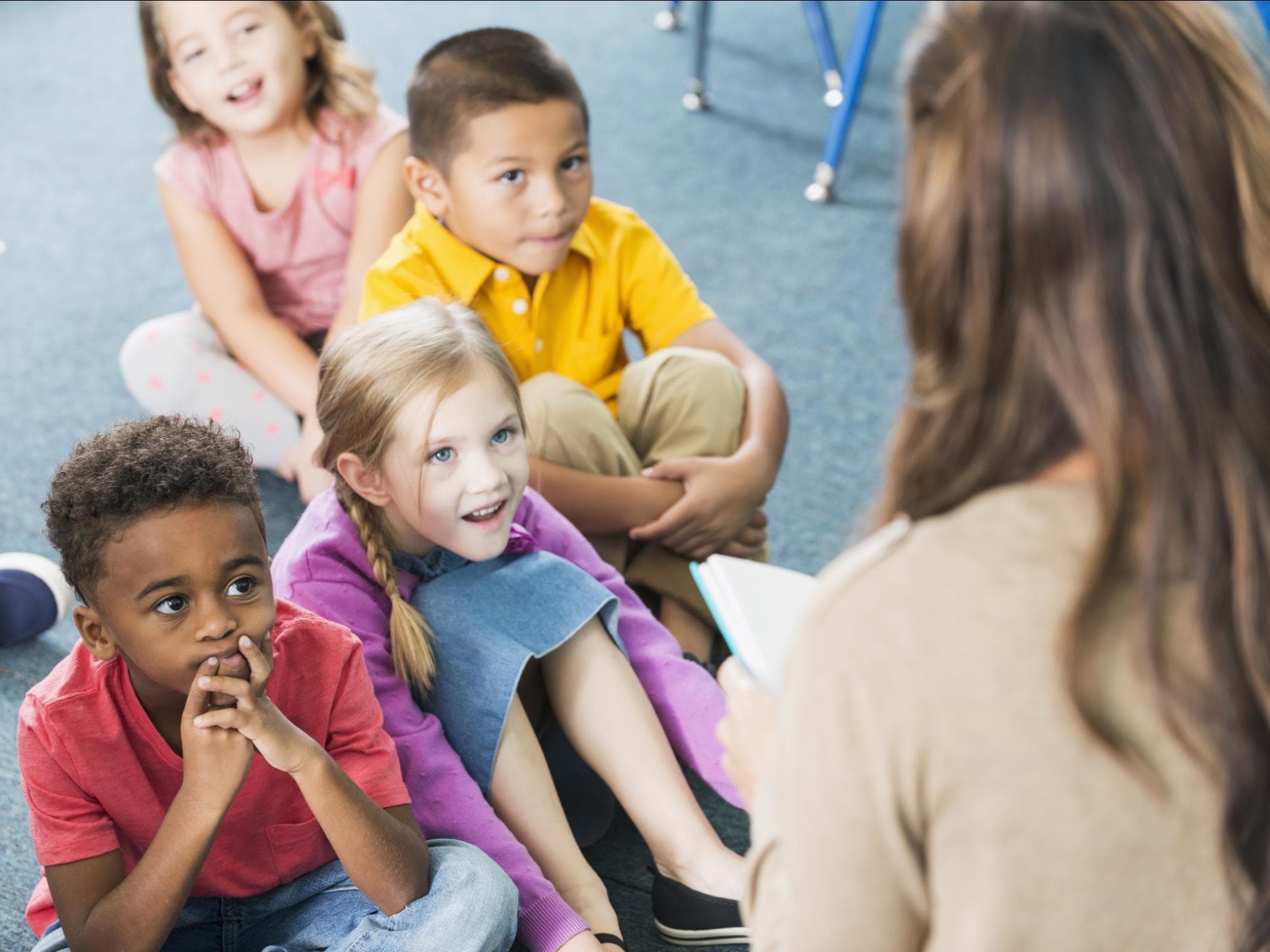 Kindergartenkinder hören einer Erzieherin beim Vorlesen zu