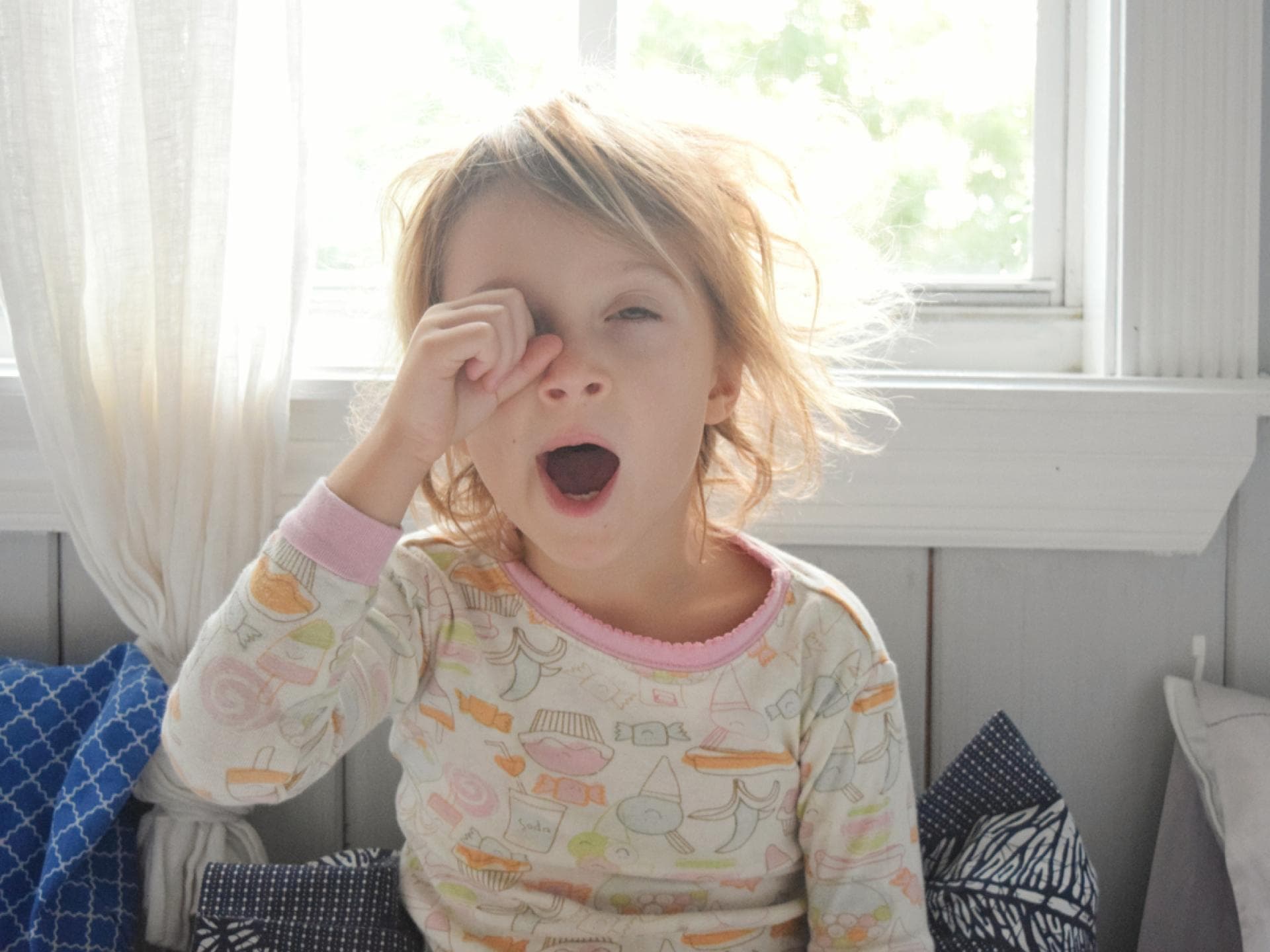 Gerade für Kinder ist die Zeitumstellung nicht immer leicht. Blondes Mädchen reibt sich am Morgen die Augen und gähnt
