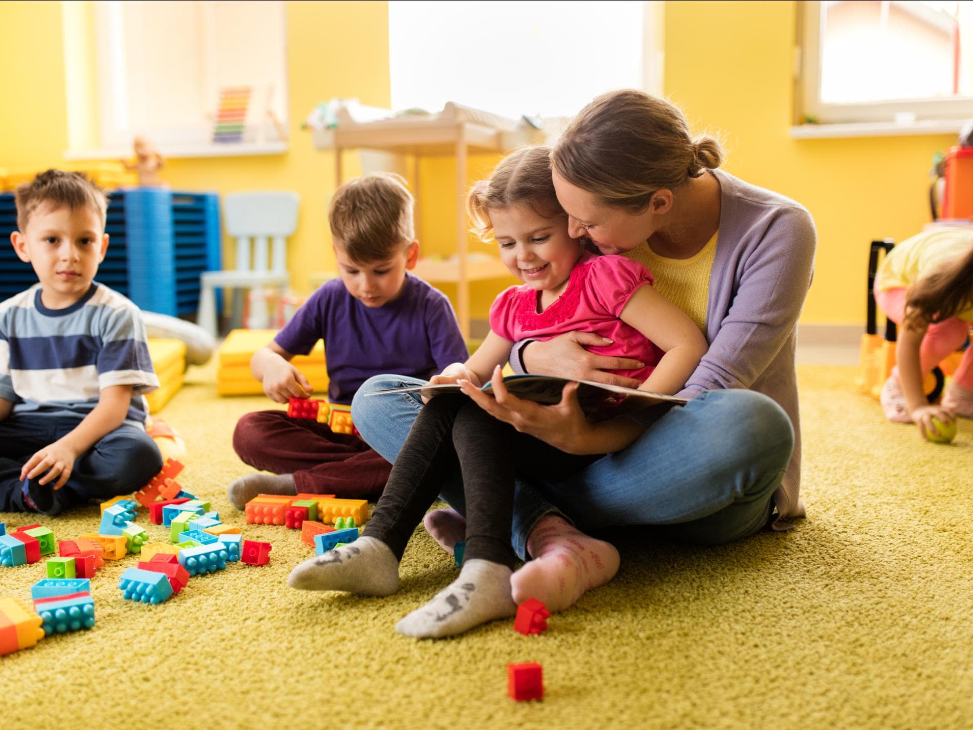 Erziehermangel in Kitas: Eine Blitzausbildung als Maßnahme gegen den Personalmangel Erzieherin liest einem Vorschulmädchen ein Buch vor und beide lächeln